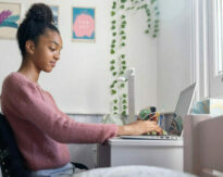 Black teenage girl doing her homework in the bedroom using her laptop computer - lifestyle concepts