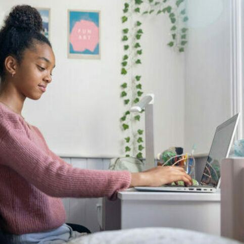 Black teenage girl doing her homework in the bedroom using her laptop computer - lifestyle concepts