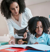 Math, education or teacher helping a child in a classroom with learning development, growth or studying. Writing, notebook or black woman teaching, talking or speaking to a young African boy student